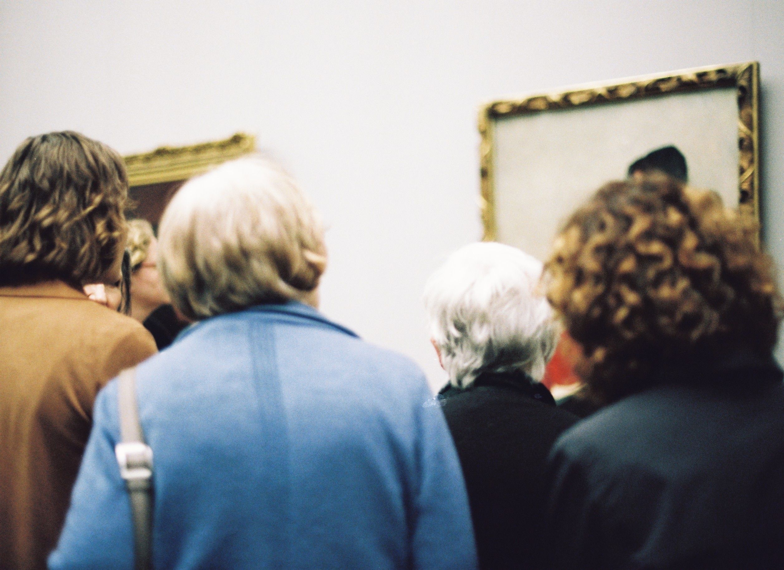 Group of adults viewing framed paintings in an art gallery exhibition